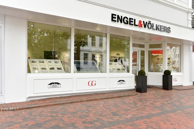 Engel & Völkers real estate office with large windows displaying property listings. Two black planters flank the entrance.
