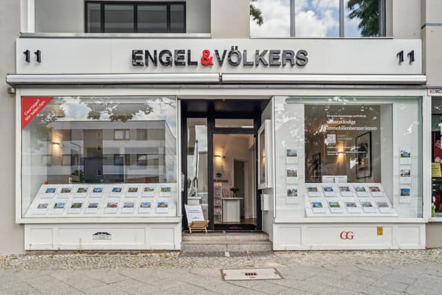 Engel & Völkers real estate office storefront with property listings in the window. The door is open, inviting customers inside.