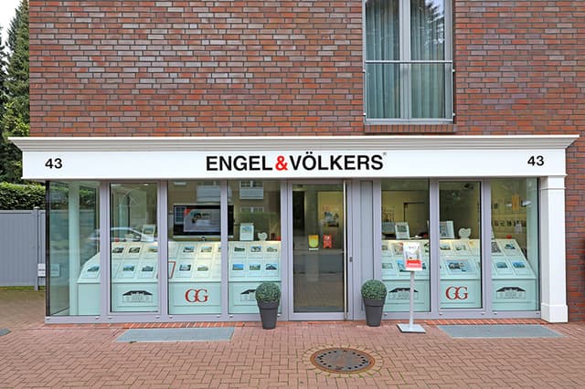 Engel & Völkers real estate office with property listings displayed in the window. The building is brick with a white trim.