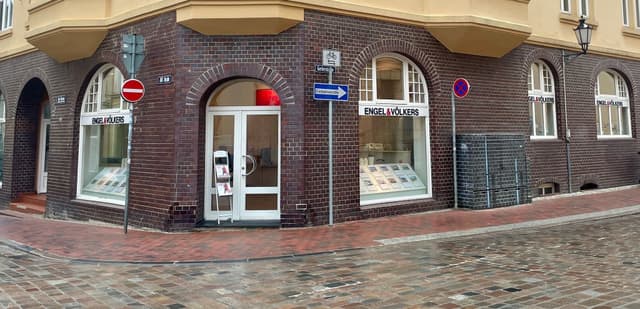 Exterior view of Engel & Völkers real estate office in a brick building with arched windows and cobblestone street.