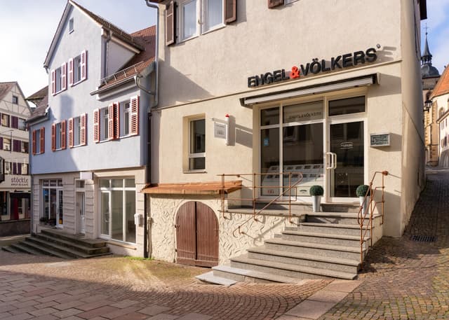 Engel & Völkers real estate office exterior. Stone steps lead to the entrance. The building has a sign with the company logo.