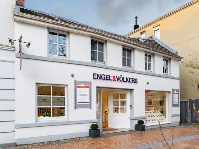 Engel & Völkers real estate office. White building with large windows, open door, and the company's name above the entrance.