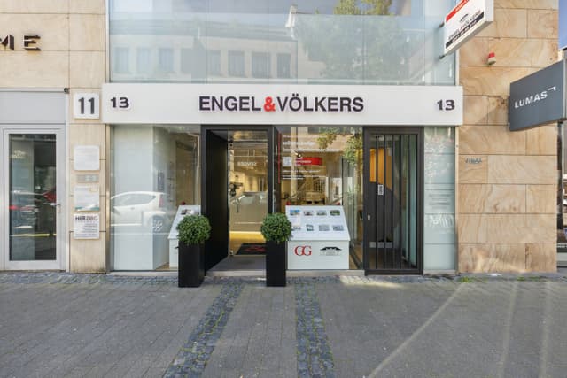 Engel & Völkers real estate office storefront with glass windows and black door frames on a stone building.