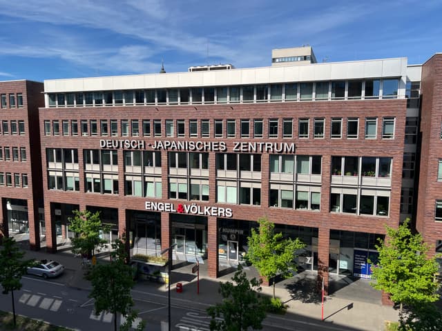 A brick building with "Deutsch-Japanisches Zentrum" and "Engel & Völkers" signs under a blue sky.