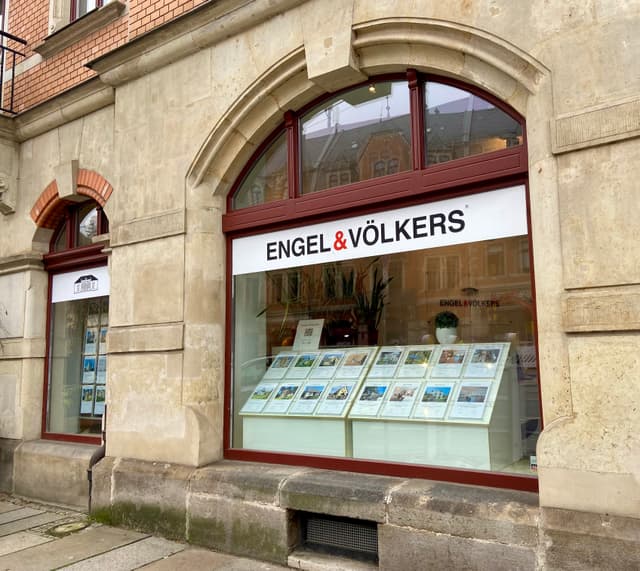 Engel & Völkers real estate office with property listings displayed in the window. The building is made of tan stone.