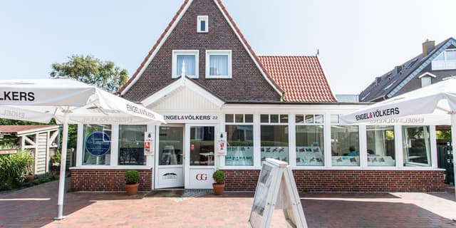 Engel & Völkers real estate office with brick facade, red tile roof, and white trim. Umbrellas with the company logo are visible.
