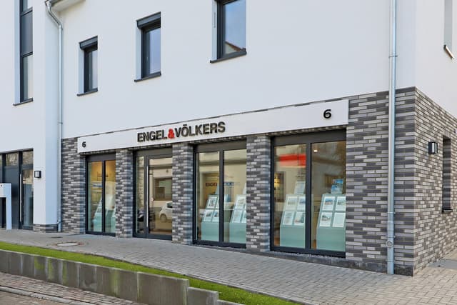 Engel & Völkers real estate office with gray brick and large windows displaying property listings.