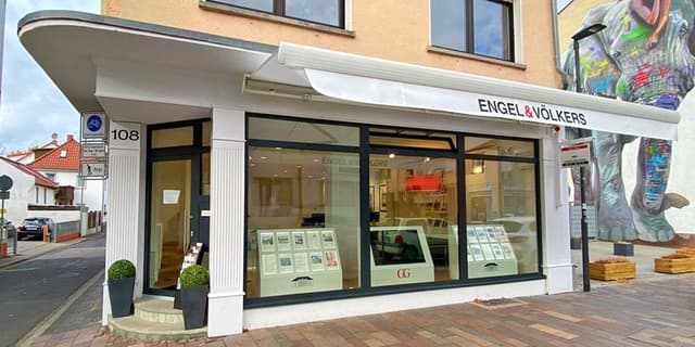 Engel & Völkers real estate office with large windows displaying property listings. An elephant mural is on the building's side.