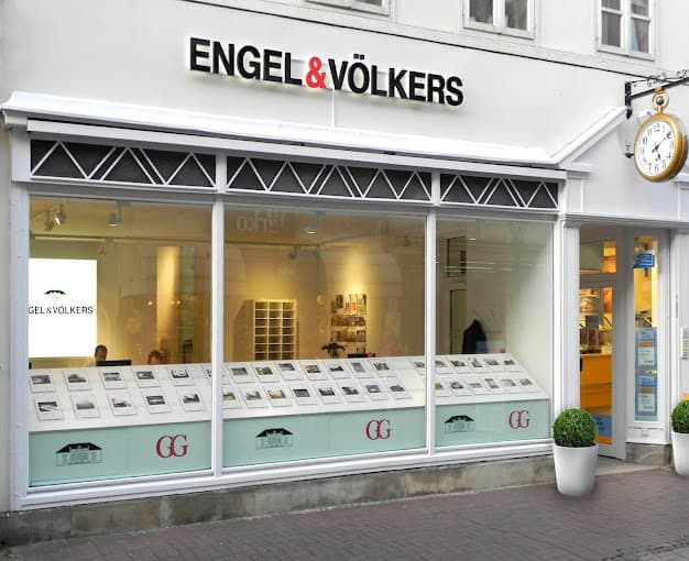 Engel & Völkers Immobilienbüro-Schaufenster mit Immobilienangeboten im Fenster. Eine Uhr hängt außerhalb des Eingangs.