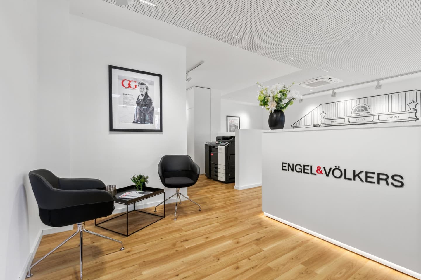 Exterior of Engel & Völkers real estate office with large windows displaying property listings and a digital screen.