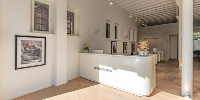 Engel & Völkers office interior with a white reception desk, wood floors, and framed art on the walls.