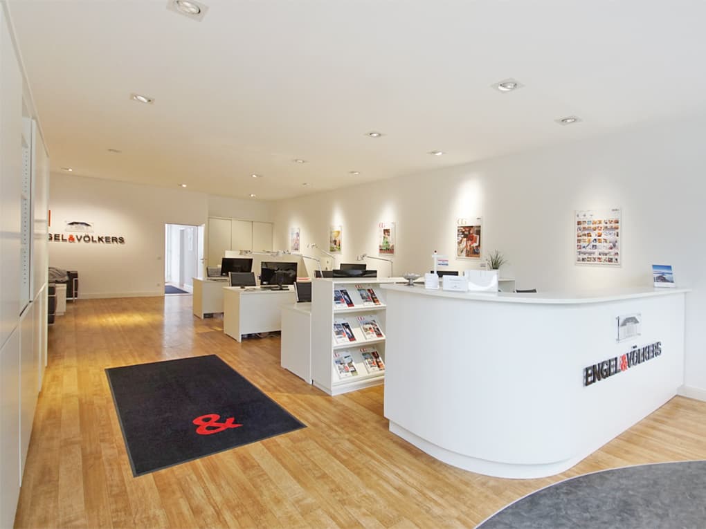 Engel & Völkers real estate office with a white reception desk, wood floors, and desks with computers.