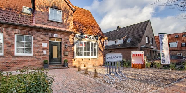 Engel & Völkers real estate office in a red brick building with a red tile roof and a beach chair in front.