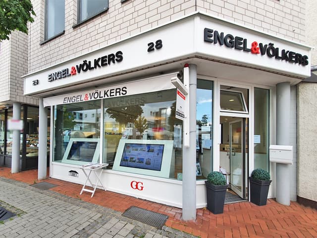 Engel & Völkers real estate office exterior with displays in the window and black lettering on a white building.