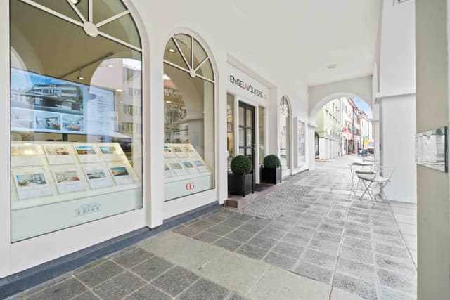 Engel & Völkers real estate office with arched windows and doorways. A table and chairs sit on the stone-paved walkway.