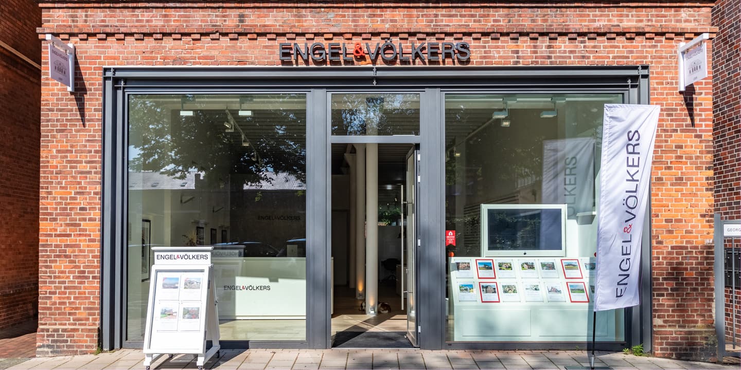 Engel & Völkers office interior with a white reception desk, wood floors, and framed art on the walls.