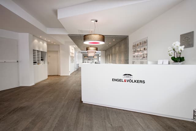 Engel & Völkers office interior with a white reception desk, wood floors, and modern lighting fixtures.