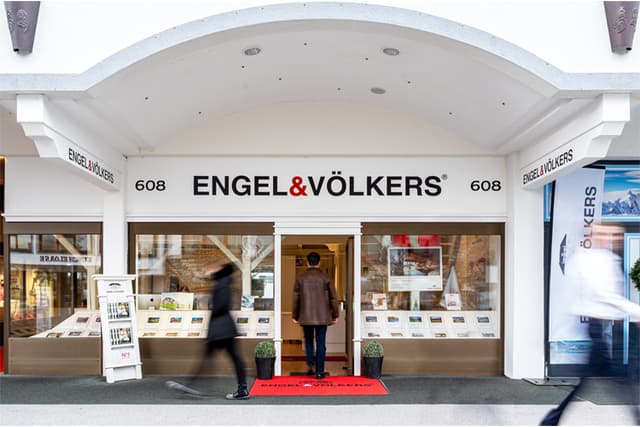 Engel & Völkers real estate office storefront with people walking by and a man entering the building.