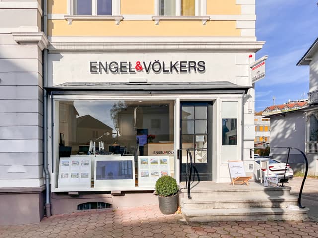 Engel & Völkers real estate office with a large window display, a black door, and a small sign on the steps.