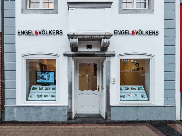 Engel & Völkers real estate office with white facade, grey trim, and window displays of properties.