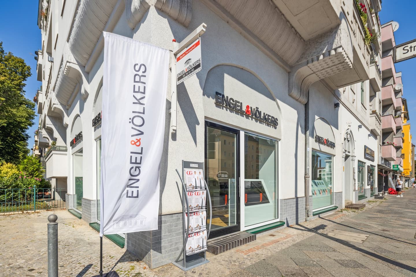 Engel & Völkers Immobilienbüro mit zwei Bogenfenstern, in denen Immobilienangebote ausgestellt sind. Weißes Gebäude mit Zierleisten.