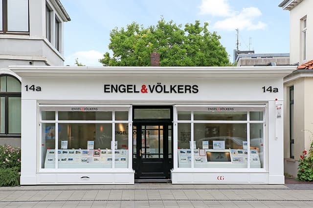 Exterior of Engel & Völkers real estate office with white trim, black door, and window displays.