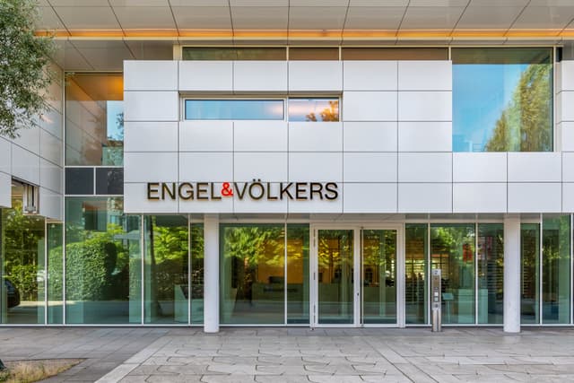 Exterior of Engel & Völkers office building with glass doors and windows. The company logo is displayed in gold lettering.