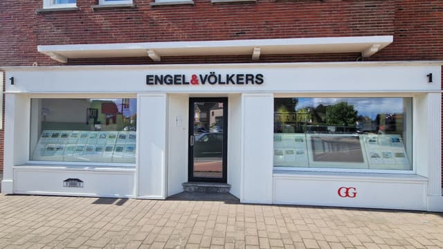 Exterior of Engel & Völkers real estate office with brick facade and white trim. Window displays feature property listings.
