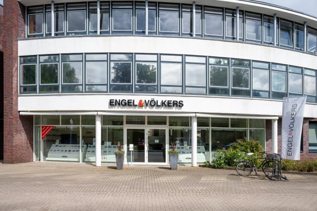 Engel & Völkers real estate office with large windows and a white sign. A bicycle is parked outside.