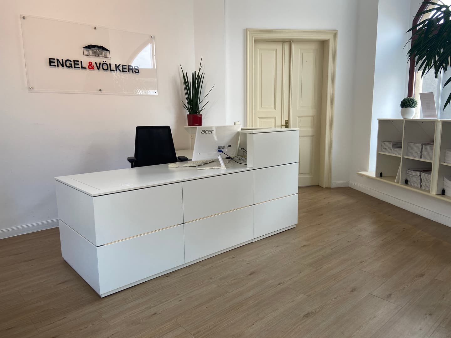 Engel & Völkers real estate office with property listings displayed in the window. The building is made of tan stone.