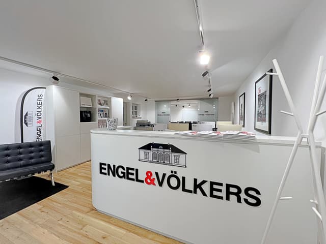 Engel & Völkers real estate office with a white reception desk, black logo, and a black leather sofa.